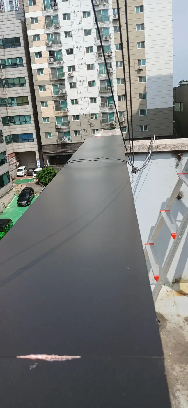 난간벽 상단을 따라 검은색 후레싱 판을 설치하는 작업 진행 모습